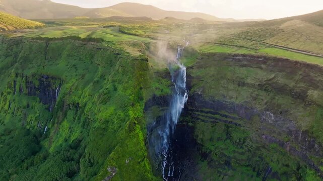 Aerial view of cascading waterfalls plunging from verdant cliffs into the abyss, a mesmerizing display of nature's power, Faj&atilde; Grande, Azores, Portugal.