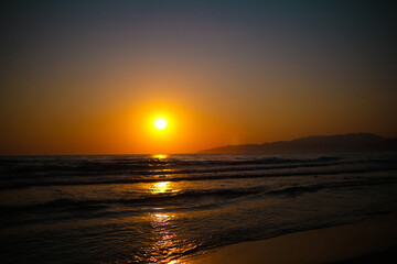 Fototapeta premium Bright orange sunset over sea with glowing light on water
