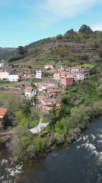 Aerial view of colorful town nestled on a hillside near a rushing river, blending textures and tones, Os Peares, Ourense, Spain.