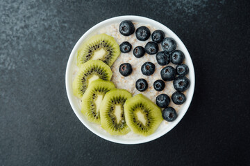Healthy breakfast bowl with kiwi slices and blueberries on dark background