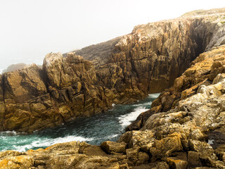 Rugged sea cliffs with misty inlet and crashing waves