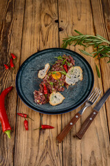 Beef tartare in a blue plate with croutons and pepper on a wooden background