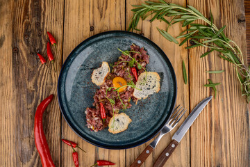 Beef tartare in a plate with croutons and pepper on a wooden background with utensils