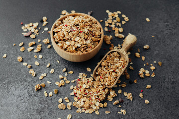 Granola bowl and scoop with scattered cereal on dark background