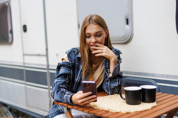 Young woman use phone in front of rented camper in vocation
