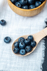 Fresh blueberries displayed in a wooden bowl and spoon on a linen cloth