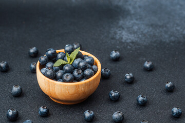 Fresh blueberries arranged in a wooden bowl on a dark surface