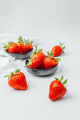 Fresh strawberries in black bowls and scattered on a light surface