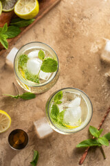 Mojito long rum drink with fresh mint, lemon juice, ice cubes and soda on brown textured background. Summer party cocktails, top view