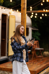 Cheerful woman smiling and browsing cellphones while chilling outside camper at night