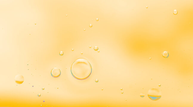Soft abstract close-up of oil bubbles floating in warm golden-yellow liquid. Transparent oil bubbles in yellow liquid background