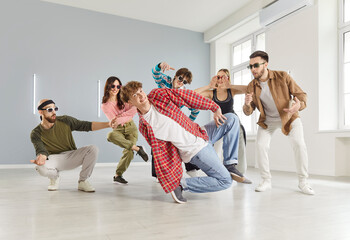 Lively group of young adults girl and guys dressed in casual streetwear, dancing energetically in a spacious, contemporary dance school studio. Hobby, fun, and urban dance culture concept