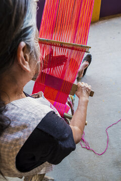 Close-up of indigenous artisan weaving red thread on a traditional backstrap loom in Oaxaca, showing craftsmanship, heritage, and cultural identity for sustainability, slow fashion and tradition.