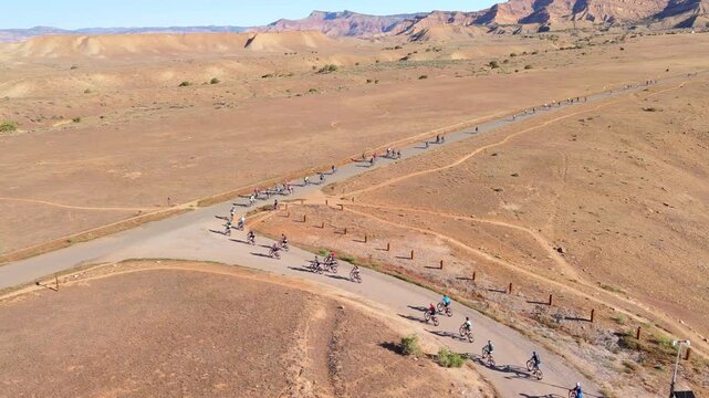 Fruita, United States - 28 July 2025: Aerial view of cyclists riding along a winding road amid the arid landscape and red rock formations.