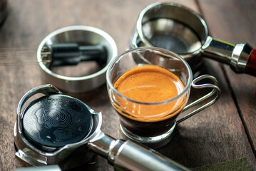 Espresso Tools: Professional Portafilter and Glass Cup with Rich Crema on Rustic Wooden Table Espresso Perfection: Dark Roast Coffee with Crema, Portafilter, and Chrome Machine Parts on Wood