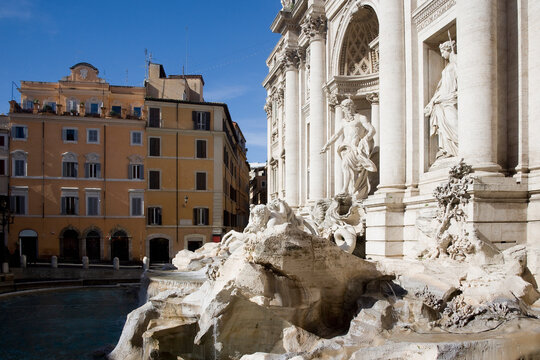 Diagonal composition of Fontana di Trevi in Rome under bright daylight with partial shadows, highlighting sculptural richness and classical elements in a lively Roman piazza setting.