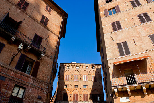 in Siena, Tuscany, under strong blue sky, showing symmetry, medieval brick texture and civic pride reflected in preserved urban fabric of central Italy.