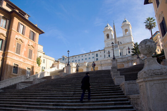 Stairway at Piazza di Spagna in Rome with a single pedestrian walking upward under clear morning light, blending monumental urban scale with human solitude and spatial symmetry.