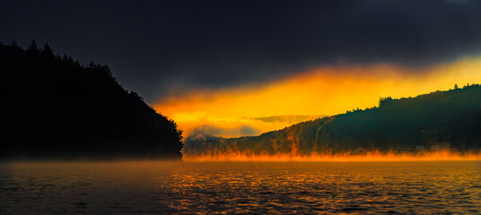 Sunrise landscape over Lake La Ravi&egrave;re in the South of France in Occitanie.
Sunlight reflecting on the calm waters with mist rising from the lake. Tree reflected in the water.
