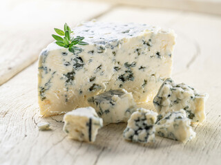 Blue cheese chunk with fresh thyme leaves on wooden table close up.
