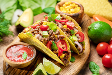 Mexican meat tacos or beef stuffed tortillas and lime slices near them on wooden serving board.