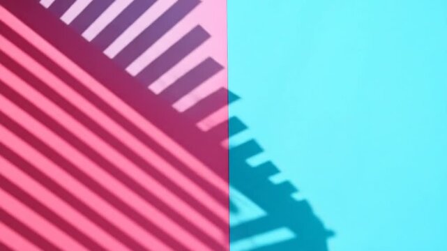 A vibrant split-screen of pink and turquoise, overlaid with a patterned shadow. The light creates diagonal stripes