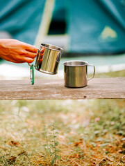 Person pouring beverage into metal cup during camping in a forest clearing