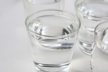 Clear drinking water in various glass cups arranged on a white surface.