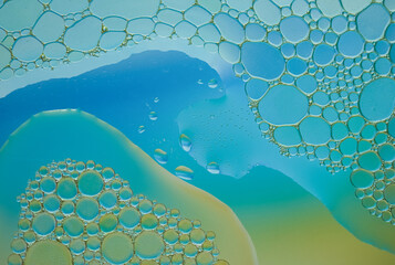 Colorful oil bubbles cluster over a green and blue fluid gradient background in macro view.