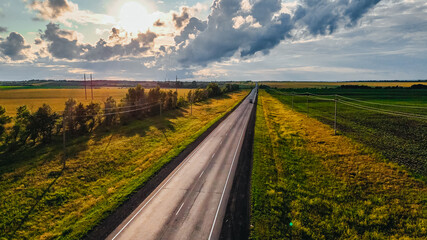 Naklejka premium cars and trucks driving along a highway in the middle of green fields at sunset