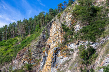Picturesque rocks covered with coniferous forest against a blue sky with white clouds.