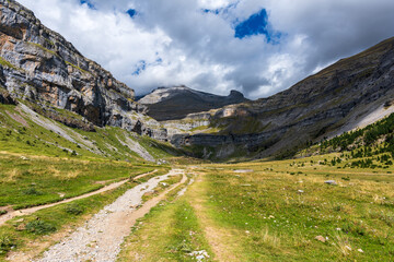 Mountain trail through a dramatic valley under a cloudy sky in late summer. Scenic mountain trail to waterfall in GR11, Ordesa National Park under a shifting sky.