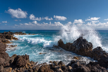 Ocean waves crashing against black volcanic rocks, dramatic spray