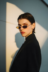 Stylish individual poses confidently in sleek attire with modern sunglasses during golden hour in an urban setting