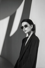 Stylish young woman with short hair poses confidently in a modern, minimalist space during bright afternoon light, showcasing monochrome fashion and striking shadows