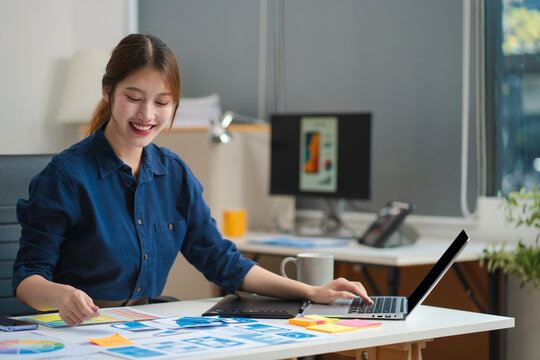 Female coder or developer working using a computer display and smartphone in problem solving at workplace.