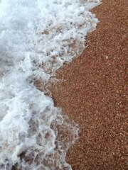 Foamy sea wave on a red pebble beach
Close-up of sea foam washing over reddish pebble sand on a Montenegrin beach, vertical composition with contrasting textures of water and stones.