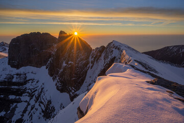View of sunrise paints the snowy mountain peaks in hues of orange and gold, a stark contrast to the cool blues of the distant horizon, Olympos, Karpathos, Greece.