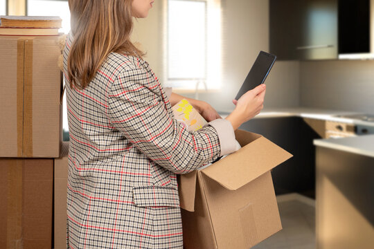 Woman with moving box. Girl carries things into empty room. Female with box in apartment. Cropped lady is engaged in moving. Relocation to improve housing. Woman calls moving specialists via phone