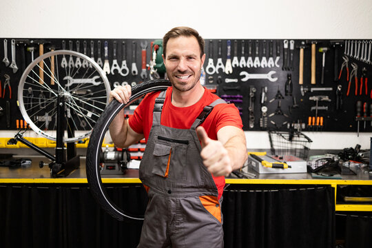 Portrait of experienced caucasian serviceman holding new tire inside bicycle workshop.