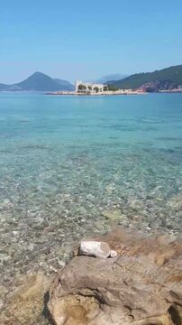 View near Cape Arza in Montenegro: crystal-clear turquoise water, the historic Žanjic Monastery on the island and surrounding scenic mountains. A slow travel moment combining nature and culture
