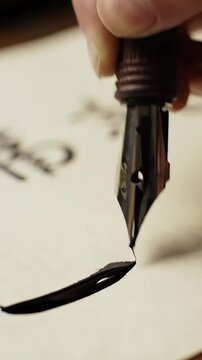 A calligraphers hand delicately dips a nib pen into an inkwell, preparing to write&mdash;crafting a single, graceful stroke with fluid, elegant precision.