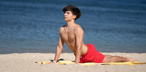 Teenager performing upward facing dog pose on sandy beach stretching before exercising enjoying healthy lifestyle with copy space