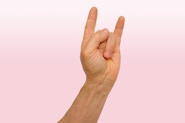 male hand on pink background, rock on sign, showing rock and roll horns gesture, strong and expressive, symbolizing strength, determination, or showing resolve, or preparation for action
