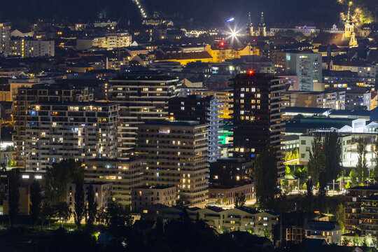 View of illuminated buildings, towers, and structures create a mesmerizing tapestry under a starlit sky, sparkling with urban light, Graz, Styria, Austria.
