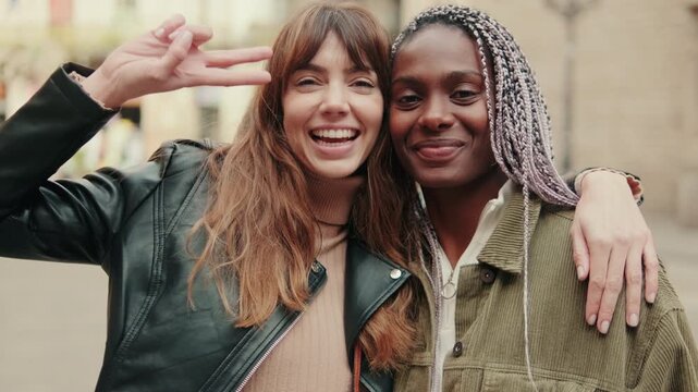 Young girls or multiethnic lesbians looking at camera showing two fingers, peace gesture, approval, friendliness, greeting or hello sign. couple hugging and laughing 