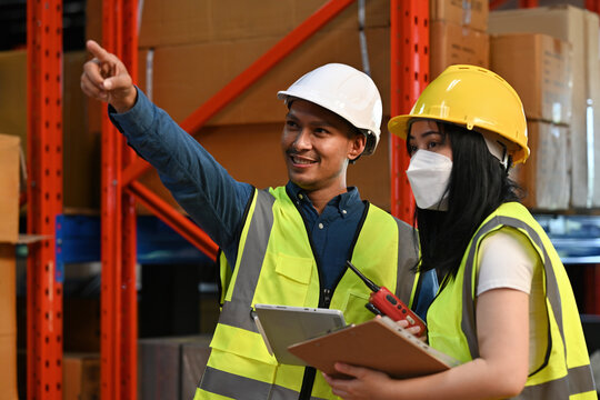 A logistics professional team discussing inventory management inside a distribution center with helmets and high-visibility vests for safety