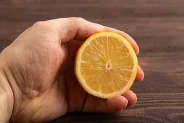 Yellow Lemon Cut in half with hand on brown wooden, Side view, close up