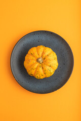 Orange Pumpkin on blue plate on orange pastel paper. Top view, copy space