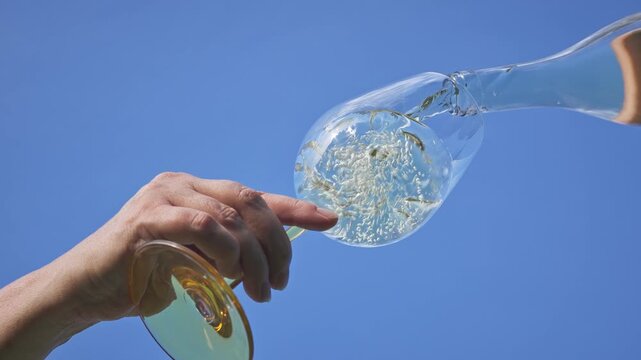fresh refreshing white wine flows into a glass from a bottle against a blue sky background, view from below, beautiful sunny summer day